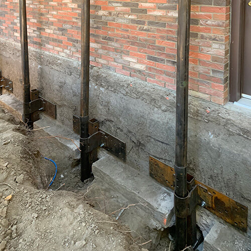 Home foundation being underpinned with screw piles